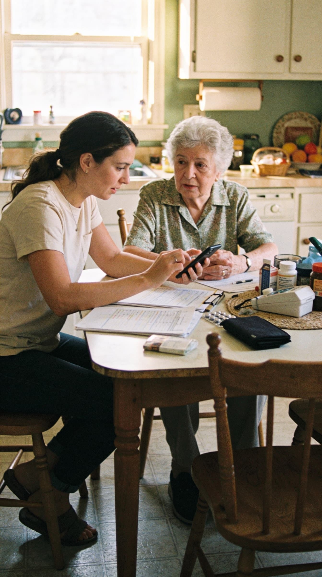 A daughter and her mother going through medications and paperwork together at the kitchen table.